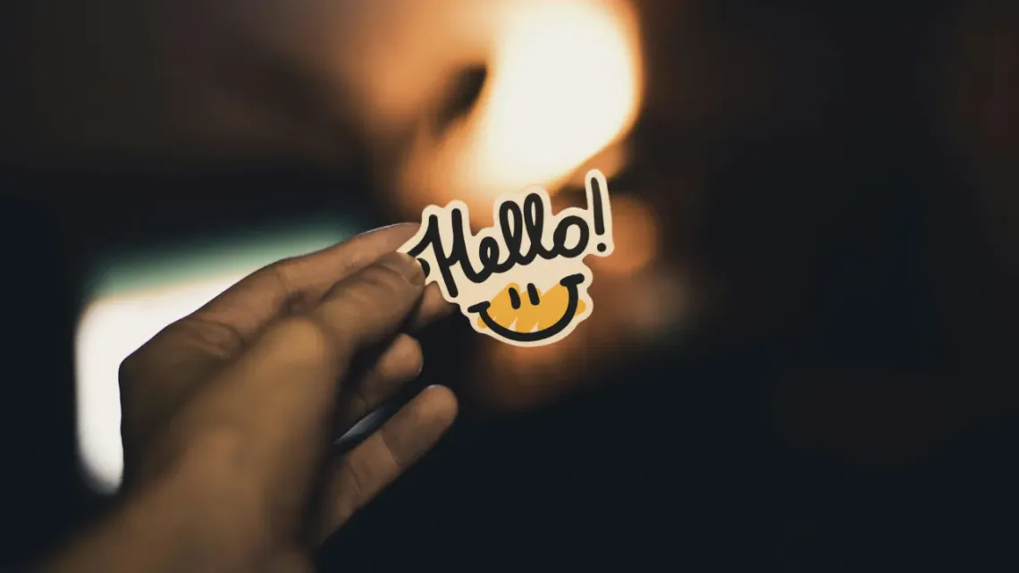 A photo of a man's hand holding a small "hello" sign.